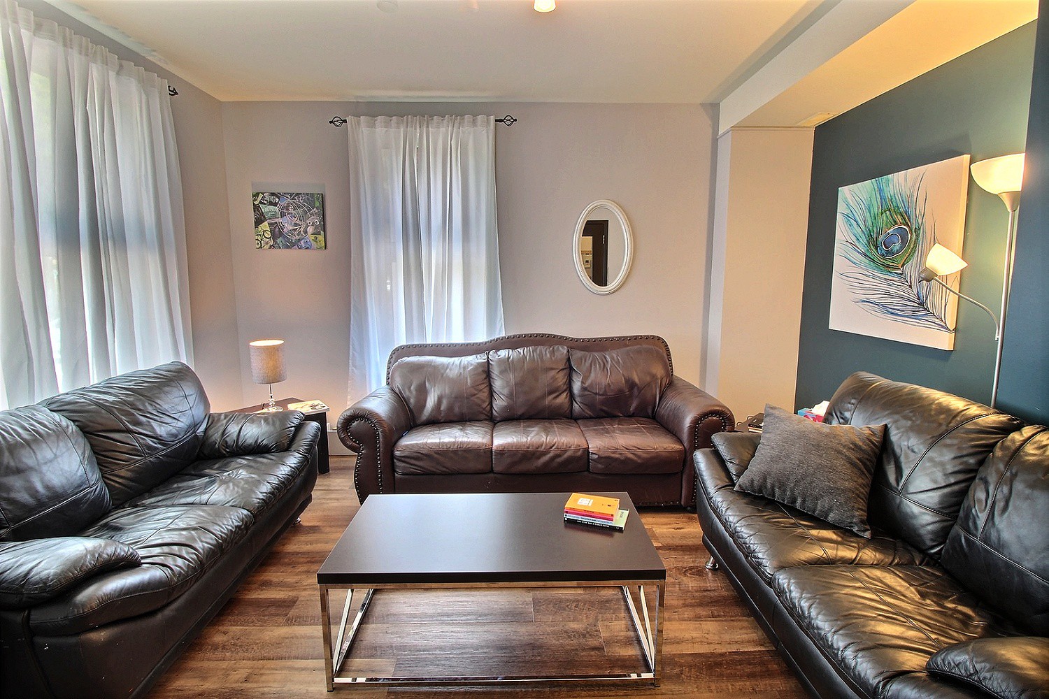 Photo d'un salon confortable muni de fenêtres, aménagé avec trois grands sofas en cuir, une table basse centrale et plusieurs luminaires.