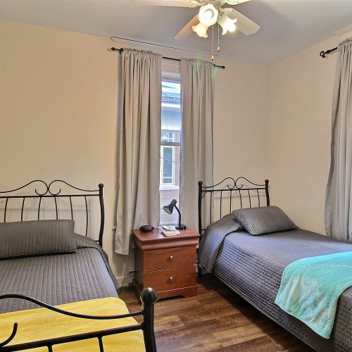 Photo d'une chambre munie de deux fenêtres, d’une table de chevet et de deux lits simples.