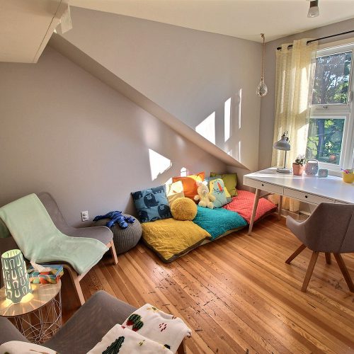 Photo d'un espace détente ensoleillé muni d’un bureau, de fauteuils confortables, de coussins et de couvertures colorés.